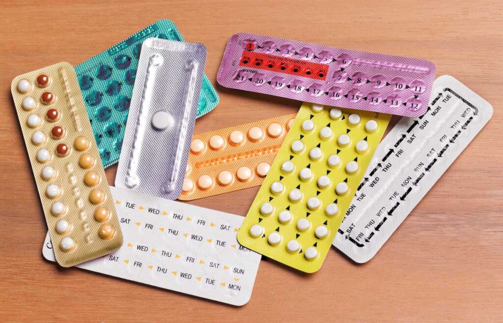 A variety of birth control pills is arranged on a wooden table.