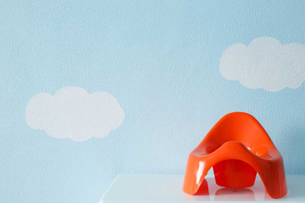 A bright red training toilet sits on a shelf in front of a light blue wall with painted clouds.