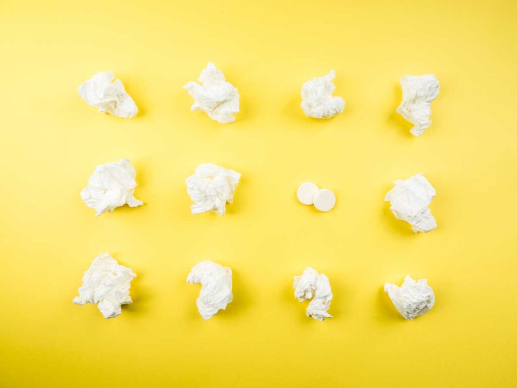 An array of used tissues and cold medicines on a yellow background.