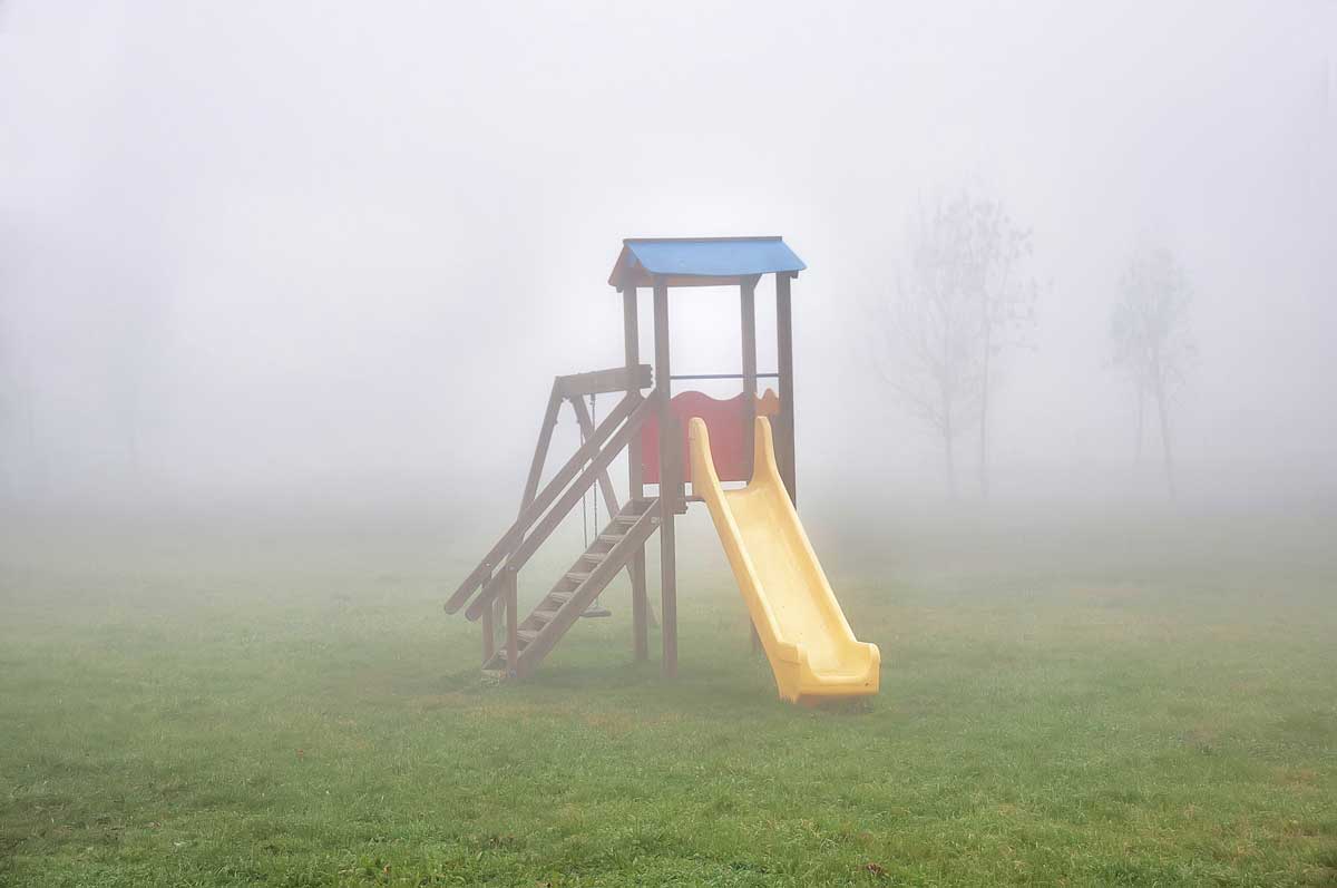 A children's slide and fort are seen, abandoned, on a smokey day.