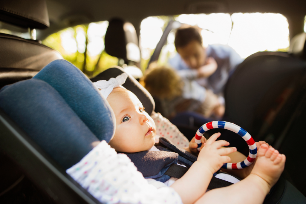 Infant wearing a bow and holding a toy in rear-facing car seat.