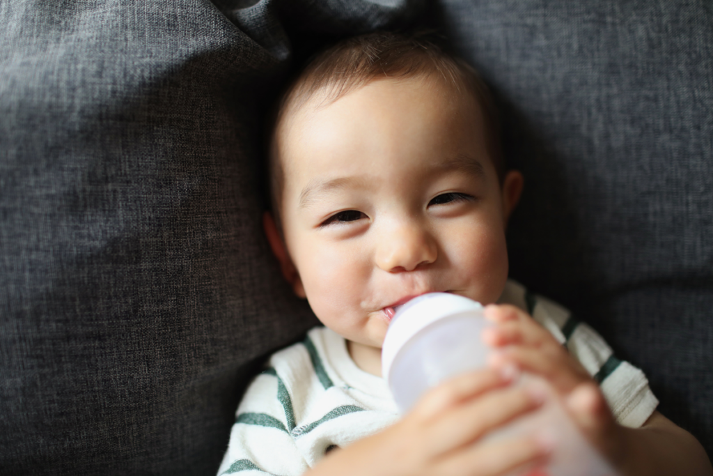 A smiling baby sips formula from a bottle.