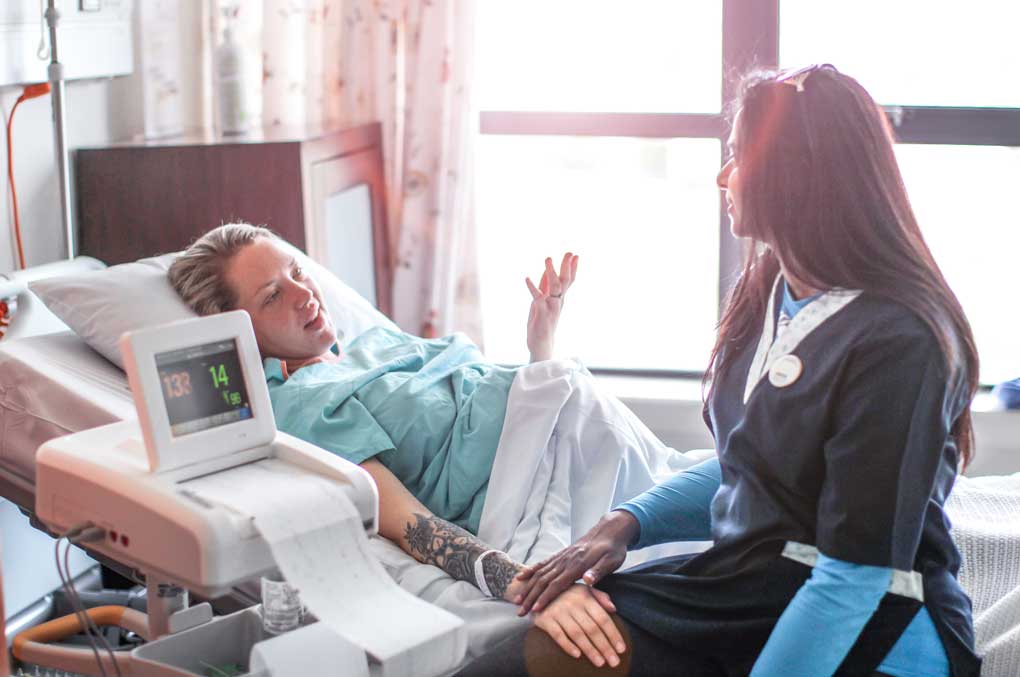 A pregnant person in labor is comforted by a doula who is guiding her through birth.