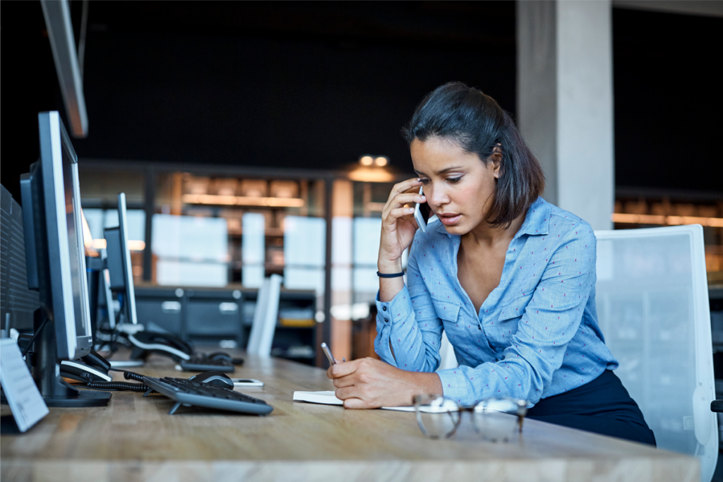 A mother looks concerned as she answers her cell phone in at her desk in an office.