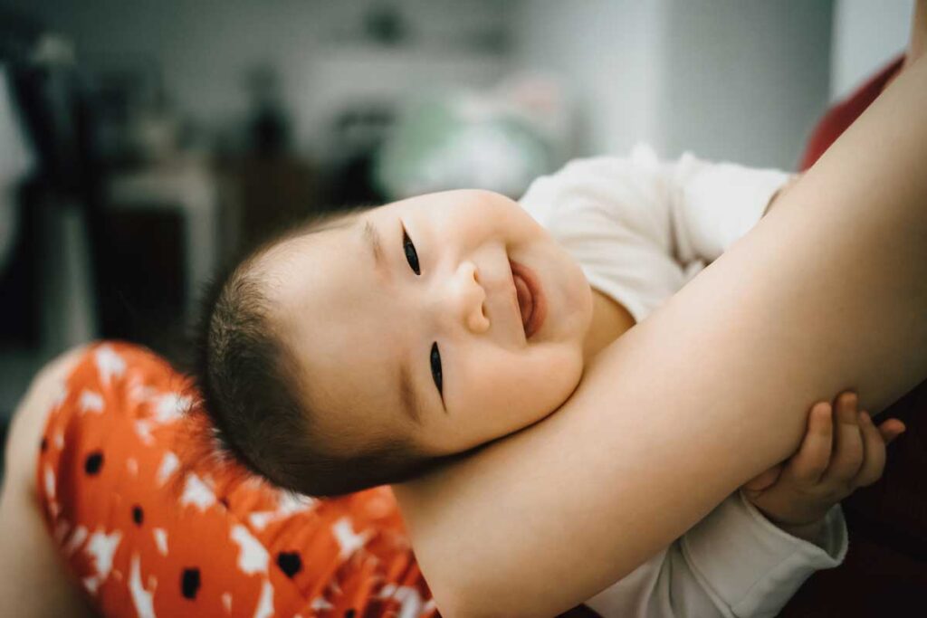 A baby smiles and tilts head while being held.