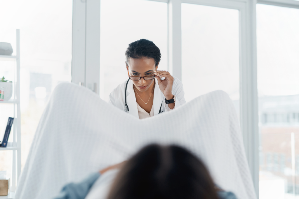 Female doctor adjusting her eyeglasses, while looking at a patient in stirrups during an exam.