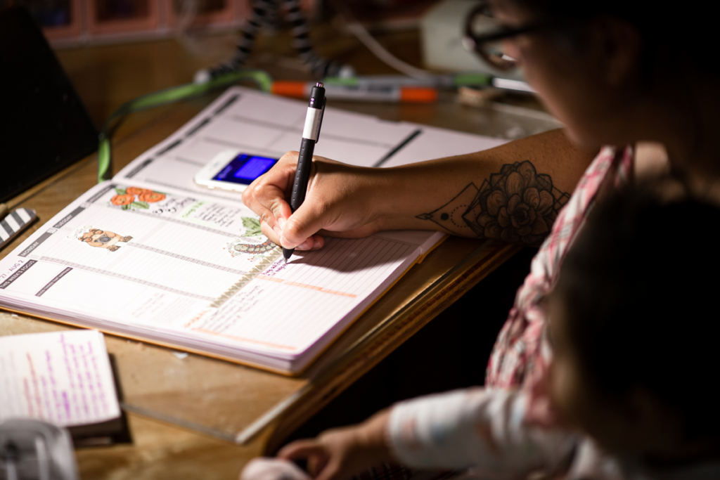 A parent holds a child while writing tasks in a planner calendar.