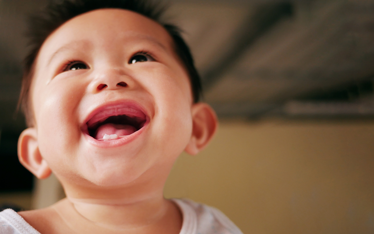 A baby with a huge smile shows off their two bottom teeth.