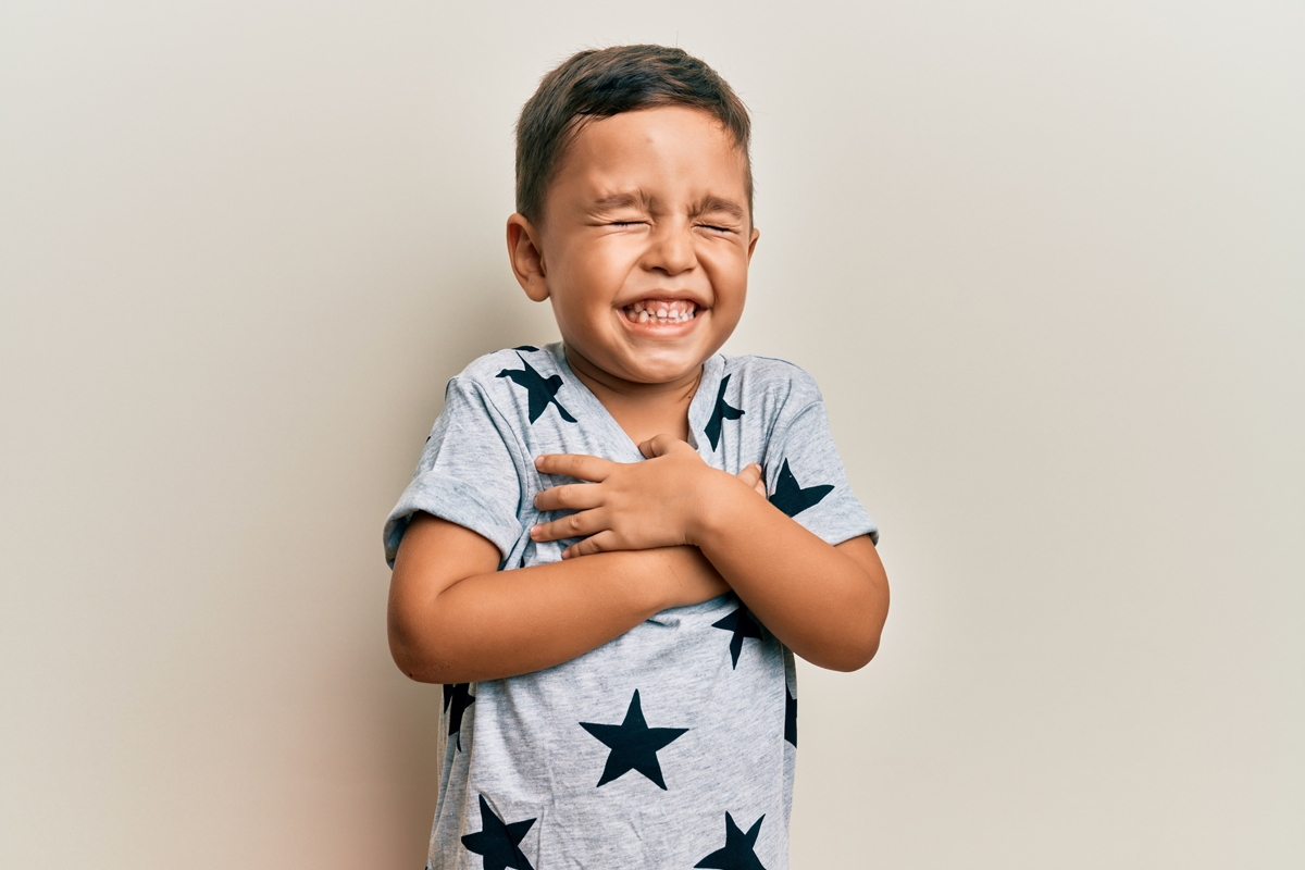 A child wearing a shirt with blue stars hugs themself and smiles as they blink.