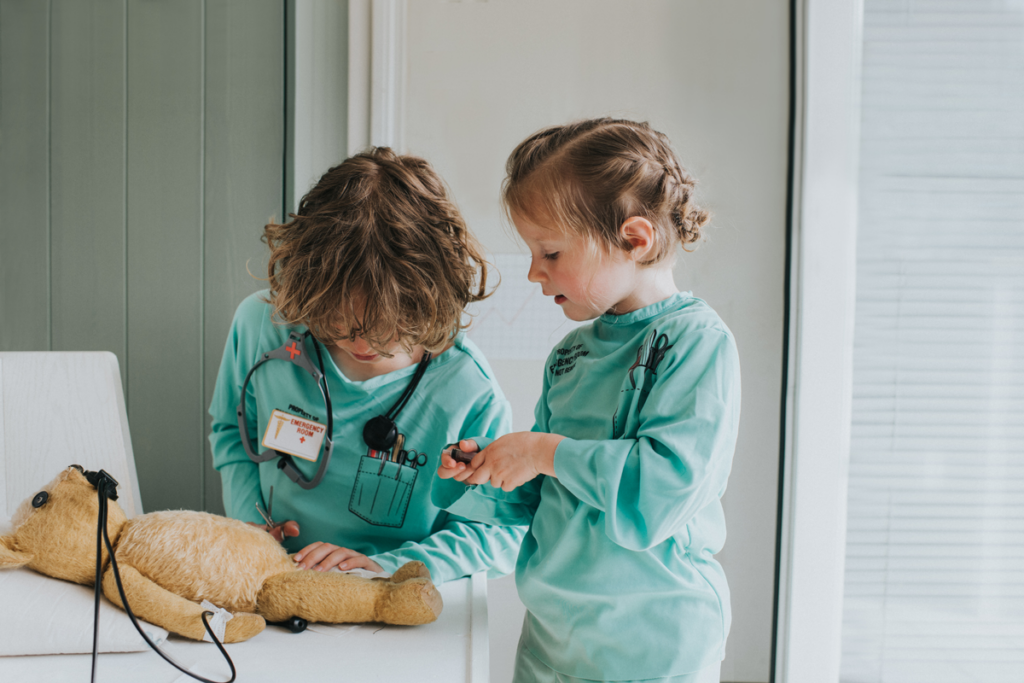 Two children pretend to give anesthesia to their teddy bear before surgery.