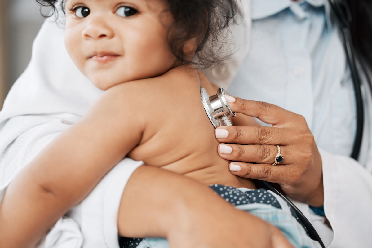 A baby smiles while a doctor listens to their lungs with a stethoscope.