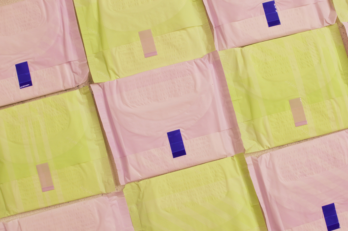 Yellow and pink menstrual pads are arranged in a checkerboard pattern.