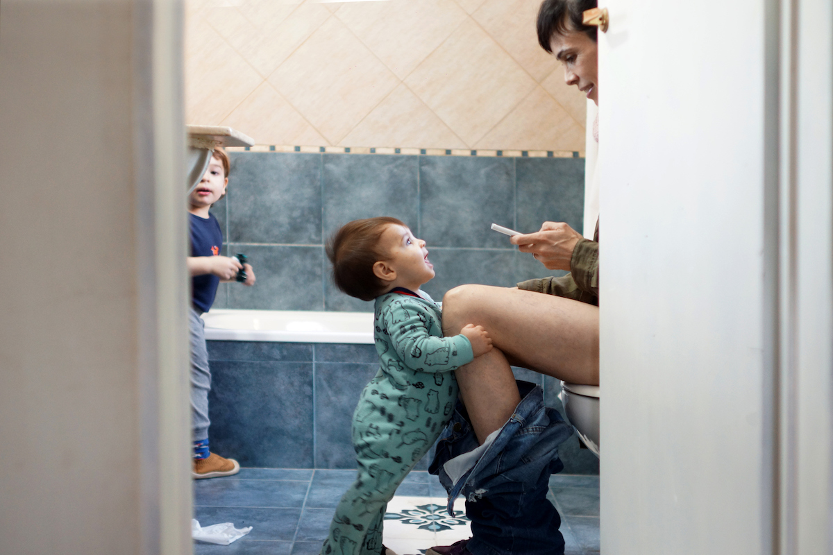 A parent reads a phone on the toilet.