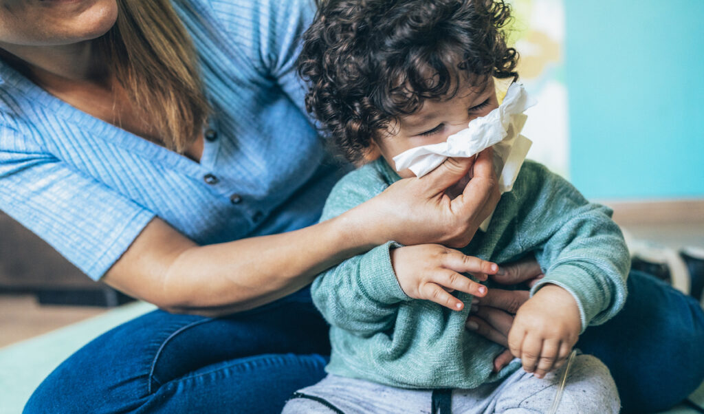 A caregiver wipes the nose of a sick toddler.