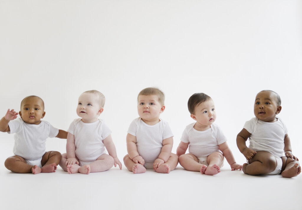 Five babies sit on the floor in a row.