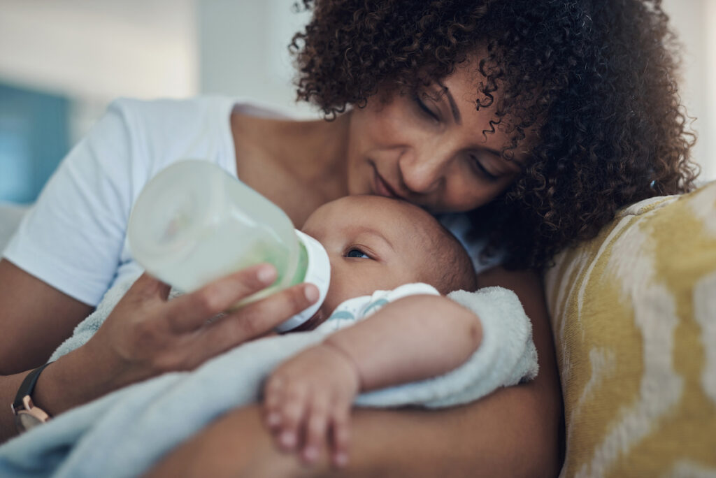 A parent cuddles with an infant while feeding them a bottle.