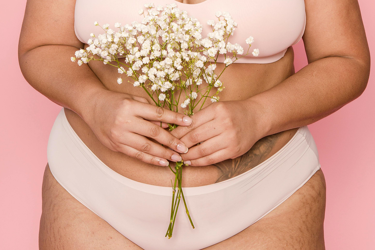 Woman in beige underwear and bra set holding a bouquet of flowers.