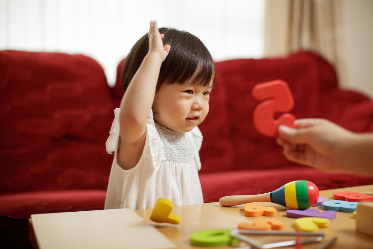 A small child learns numbers with their parent, who is holding up a red "5."