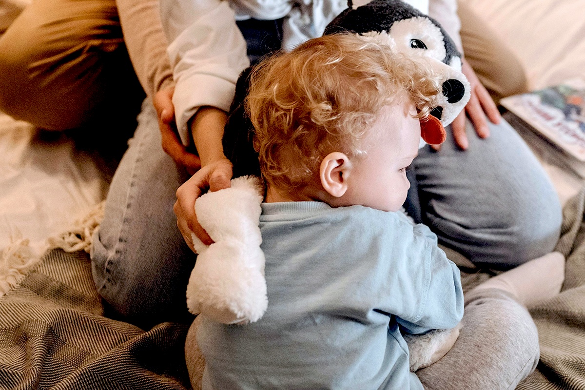 Small child laying on their parent in bed with a stuffed animal.