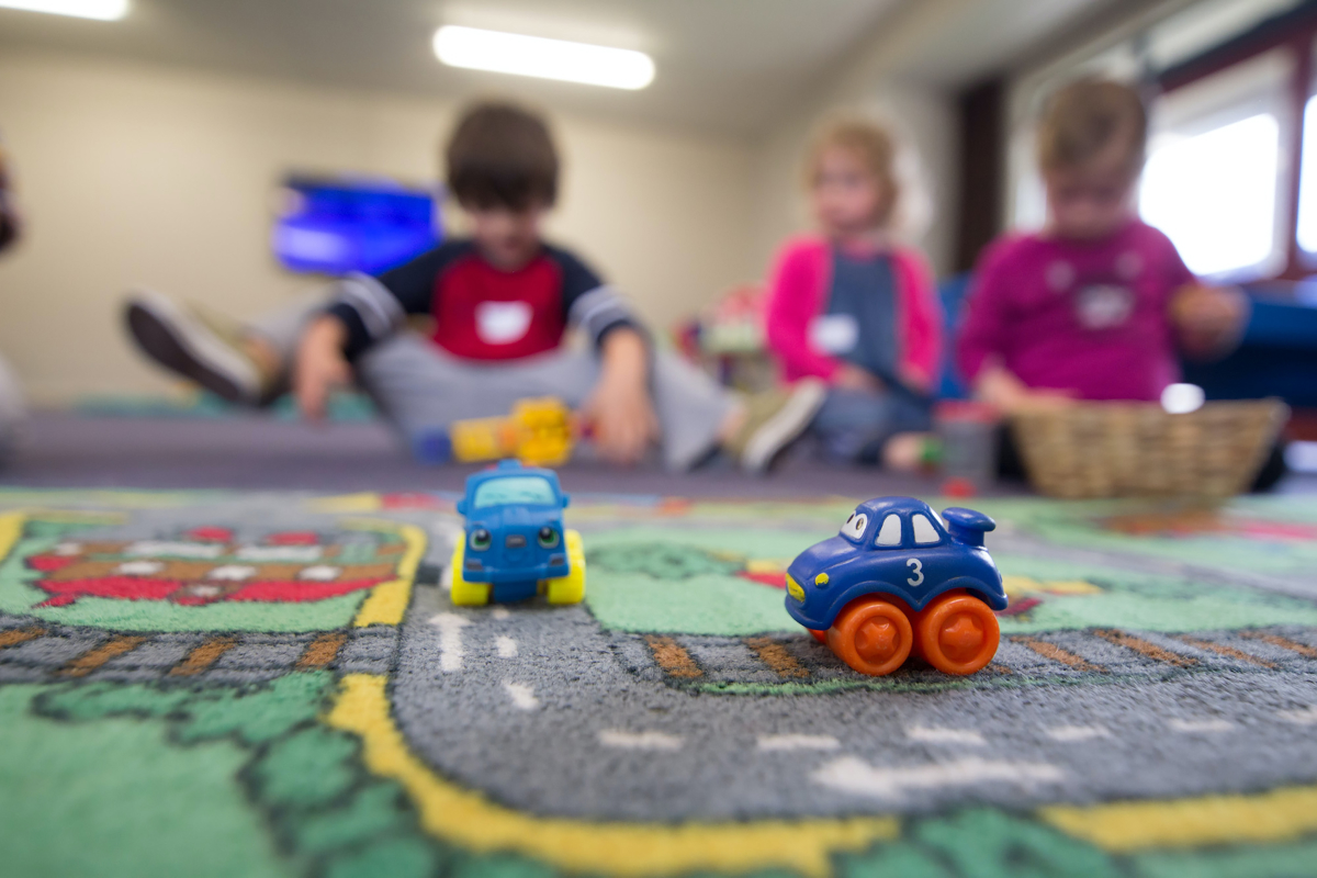 A group of children play with toy cars on the floor.