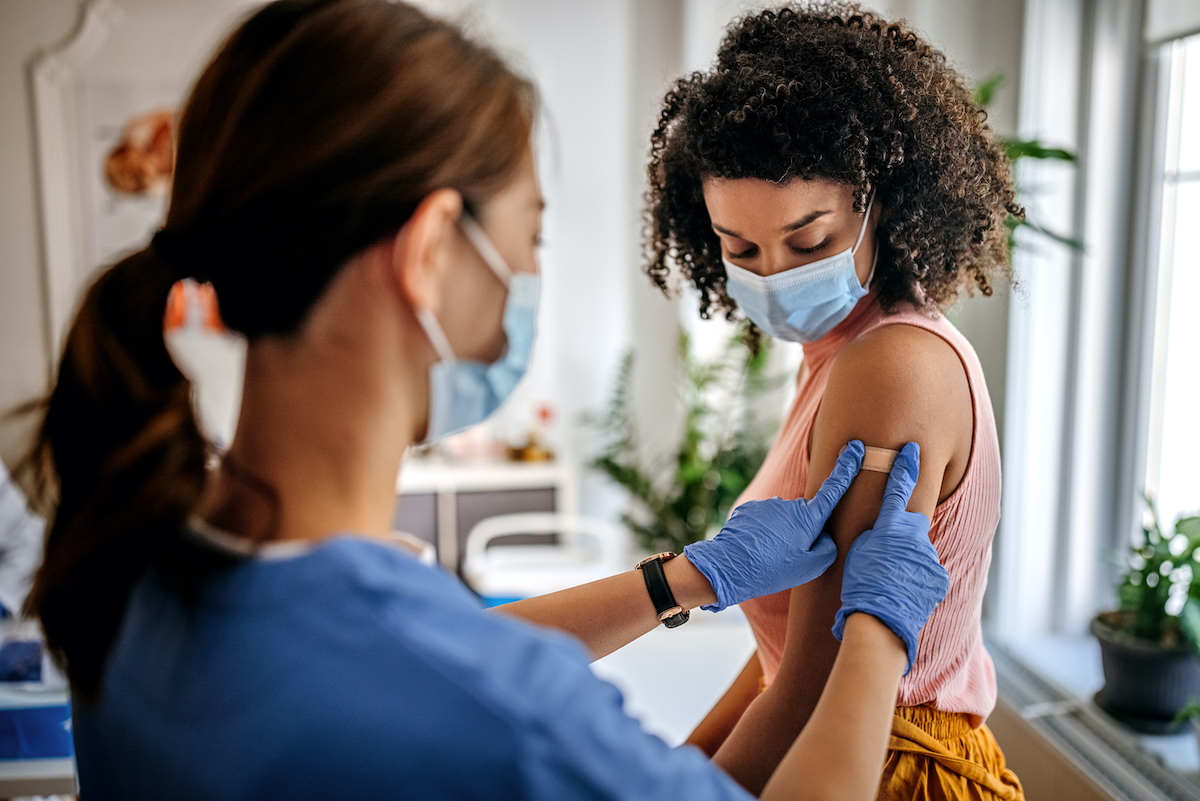 A nurse puts a bandaid on a teen's arm after administering a vaccine.