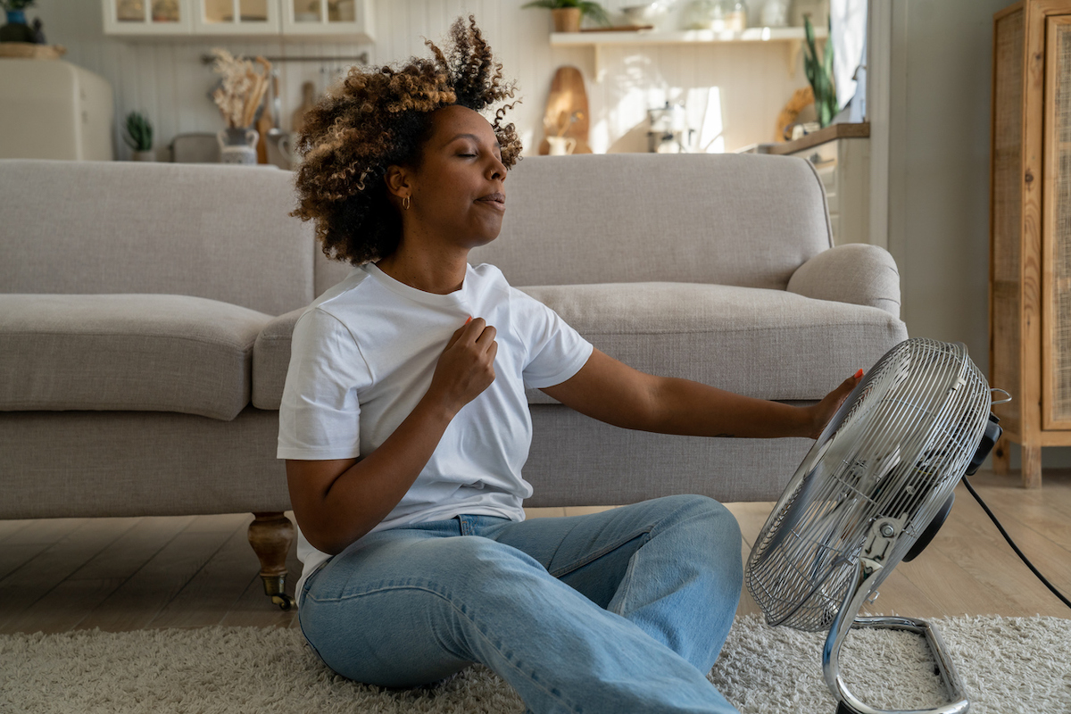 Person in a white tee shirt cools off by a fan.