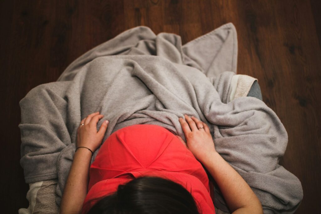 A top-down view of a pregnant person seated on a couch with a cozy blanket.