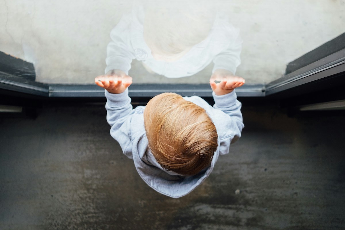 Infant standing against window.