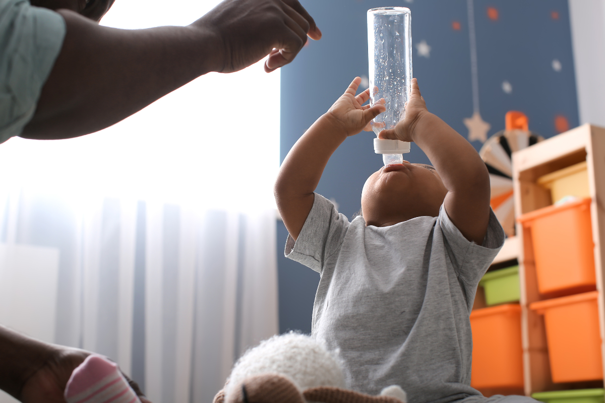 A toddler finishing milk from his bottle while the parent is trying to take it.