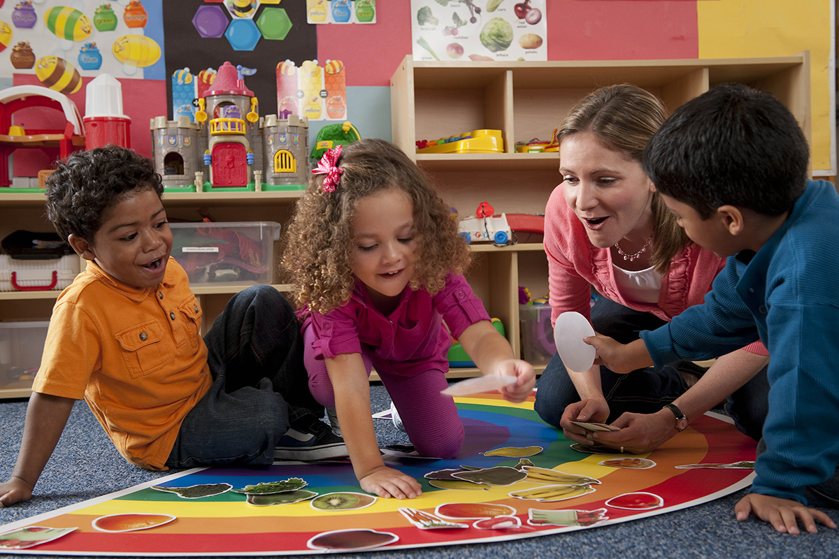 Children sort pictures of food by color in a day care center with the help of a teacher.