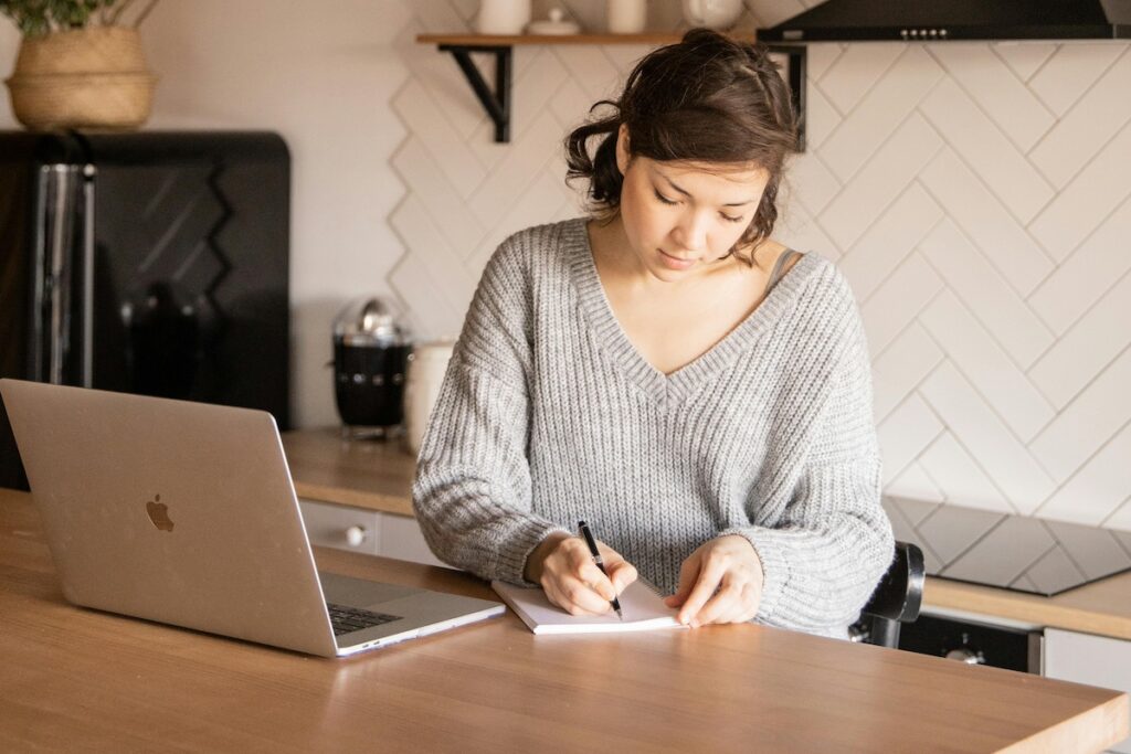 Person sitting at counter with computer and notepad