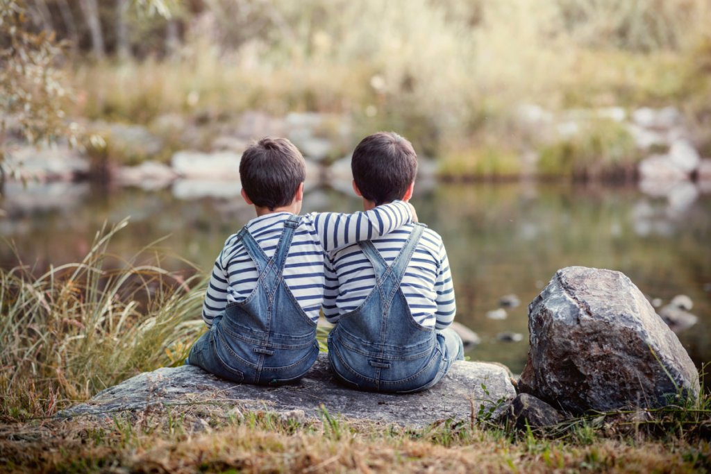 Twin kids sitting on a rock by the lake.