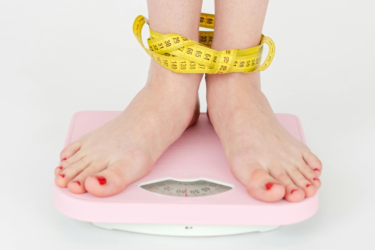 View of person's feet on scale with measuring tape around their ankles
