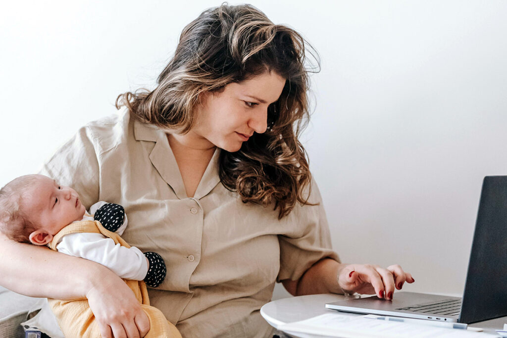 New parent holding infant while on laptop