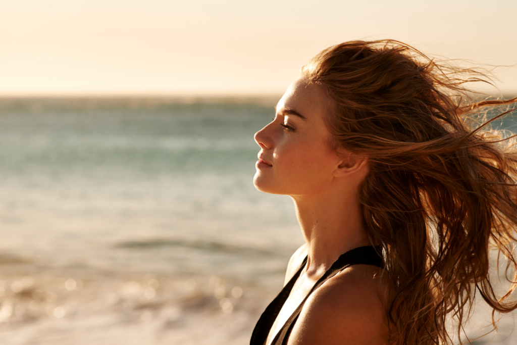 A person standing on a beach with wind on her hair