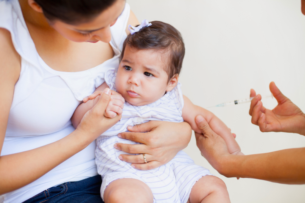 Young baby getting vaccine from nurse, while mother holds her.