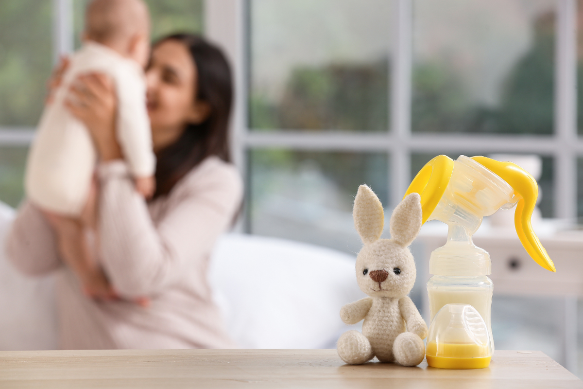 A parent holding her baby in the background with a breast pump and a bunny toy in focus