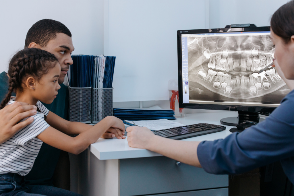 A dentist showing kid's dental x-ray to the parent and kid