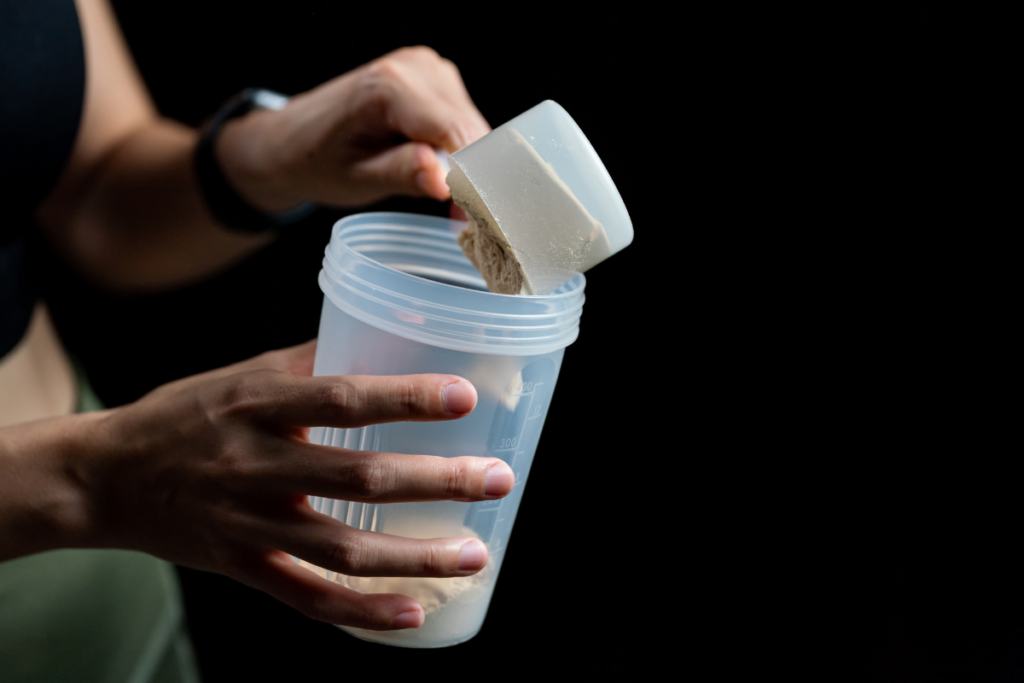 A person adding creatine powder in a blender jar.