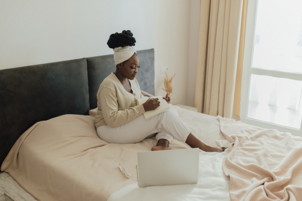 A person in bed writing something with laptop open on cushion