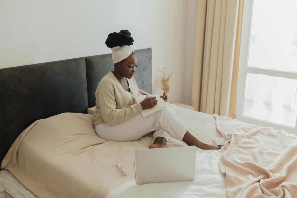 A person in bed writing something with laptop open on cushion