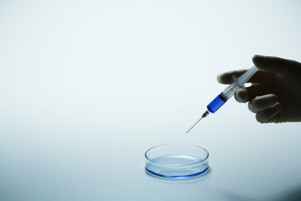 A gloved hand injecting a solution in a petri dish.