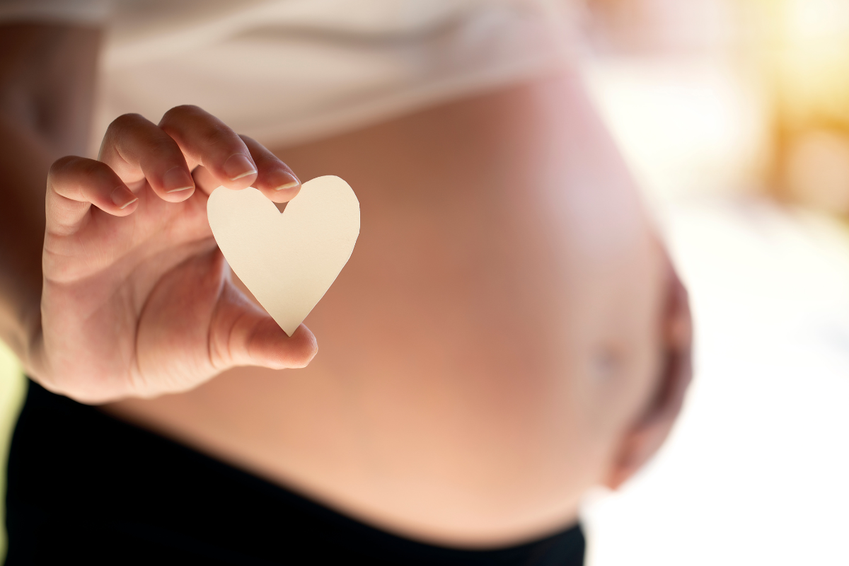 A pregnant person holding a tiny paper cut-out of heart.