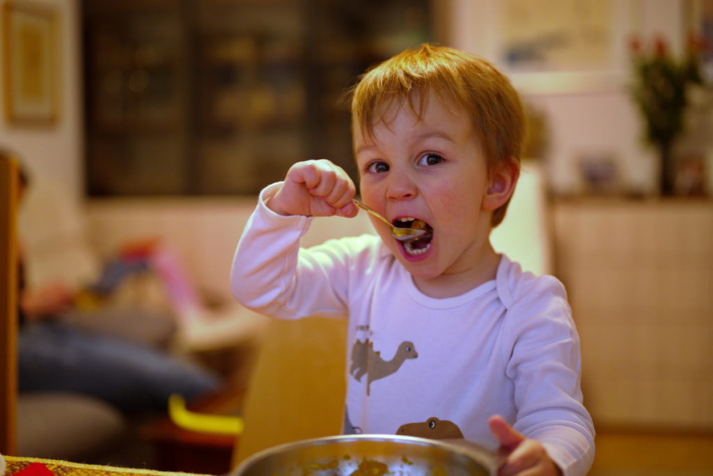 A toddler eating with a spoon.